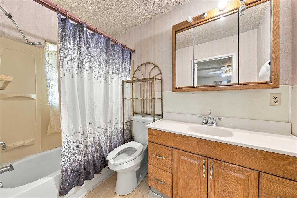 Bathroom featuring a wood-finish vanity with a molded countertop and integrated sink, a tri-fold medicine cabinet, and a combined tub and shower enclosure with a surround