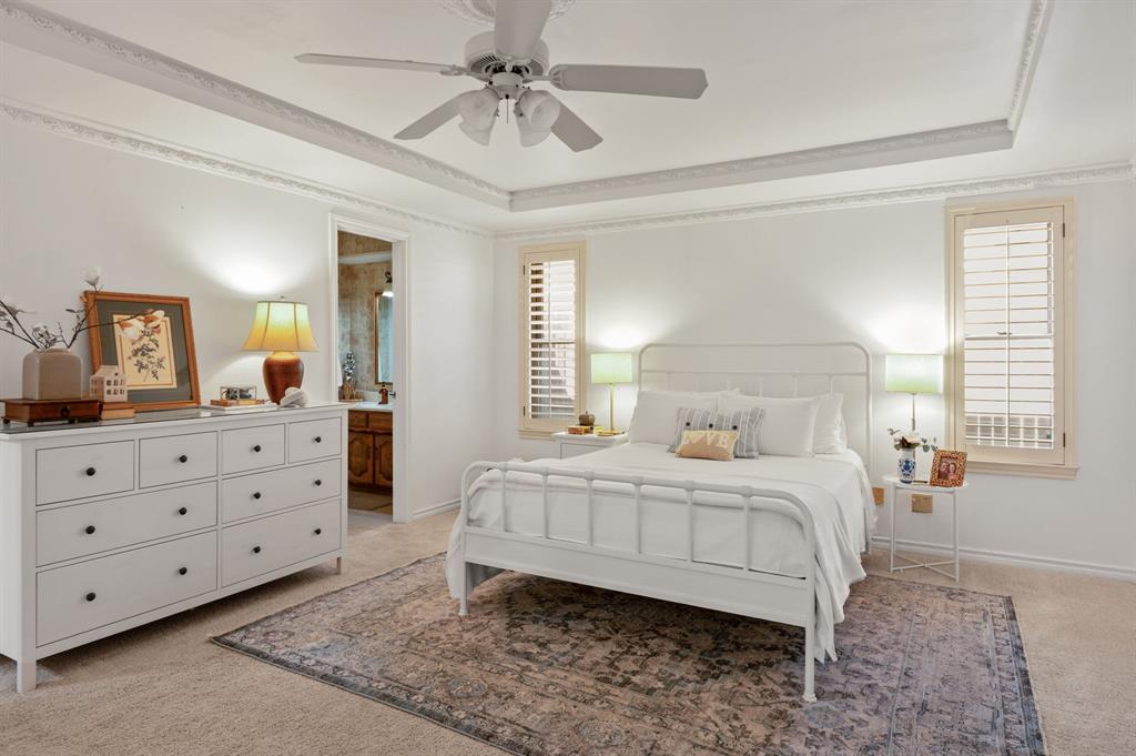 Tray ceiling with intricate crown molding, central ceiling fan, and plantation shutters