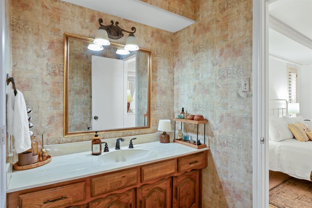 Bathroom vanity featuring a light-toned countertop, an integrated oval sink, three-handle faucet, wood cabinetry, and a large gold-framed mirror with multi-light wall fixture
