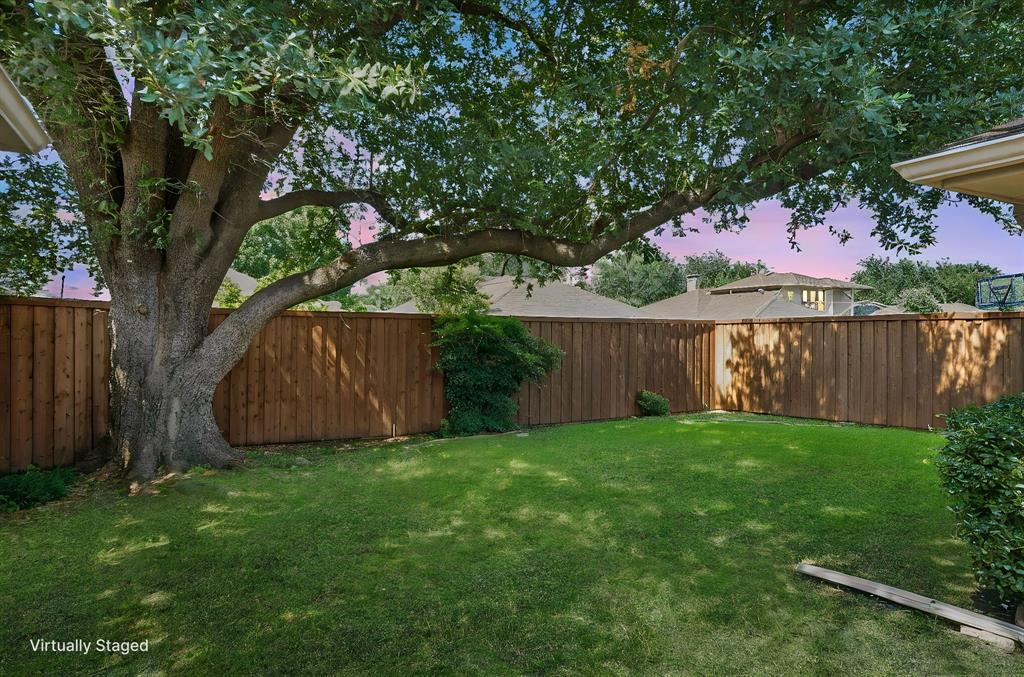 Backyard featuring a manicured lawn, mature shade tree, and wood privacy fencing