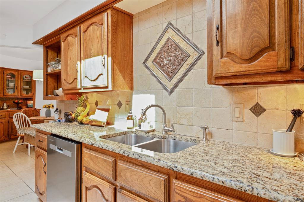 Kitchen featuring wood cabinetry, stone countertops, a dual-basin stainless steel sink with a high-arch faucet, and a decorative tile backsplash