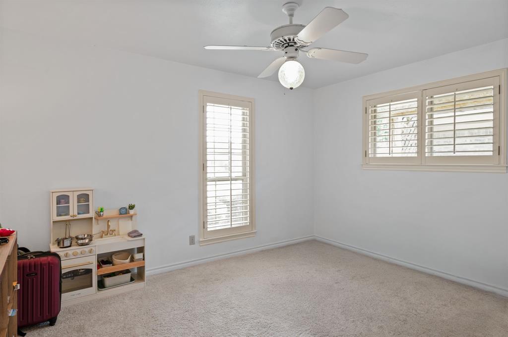 Neutral-toned interior space featuring light-colored wall-to-wall carpeting, ceiling-mounted light fixture with fan, and windows outfitted with white plantation shutters