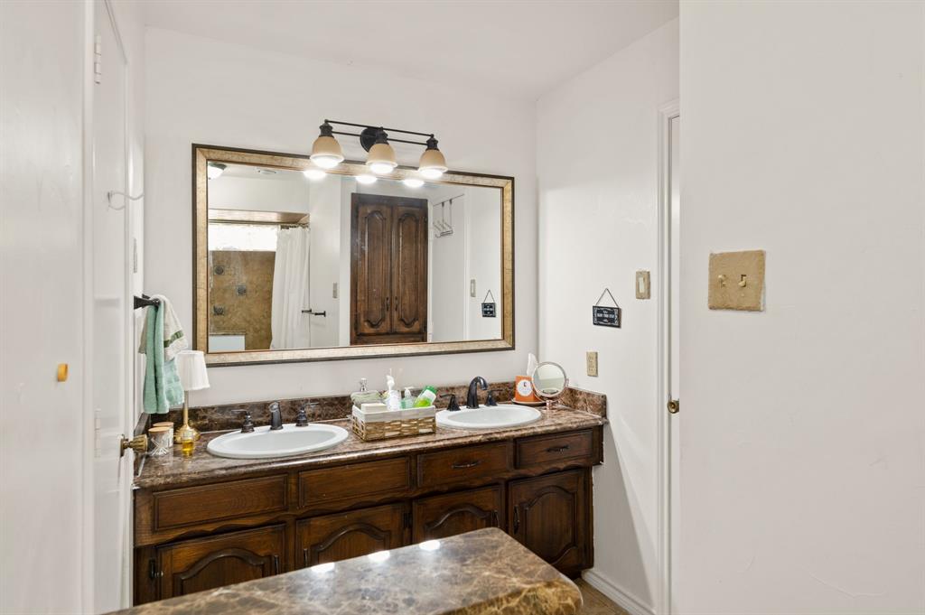 Dual-basin vanity featuring stone-finish countertops, dark wood cabinetry, integrated oval sinks, and a large framed wall mirror with a multi-bulb light fixture