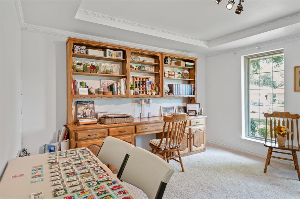 Built-in wooden desk and cabinetry featuring integrated shelving, recessed tray ceiling with crown molding, and tall windows