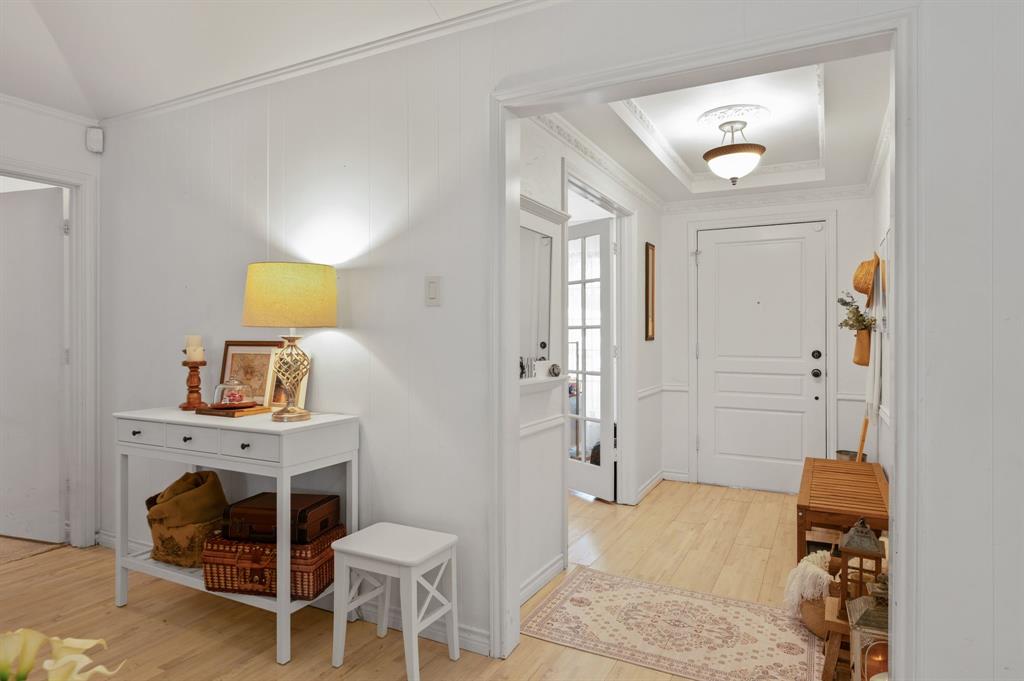 Interior entry featuring wood-finish flooring, white panel molding, a recessed ceiling tray with crown molding, a semi-flush mount light fixture with a decorative ceiling medallion, and a multi-panel door