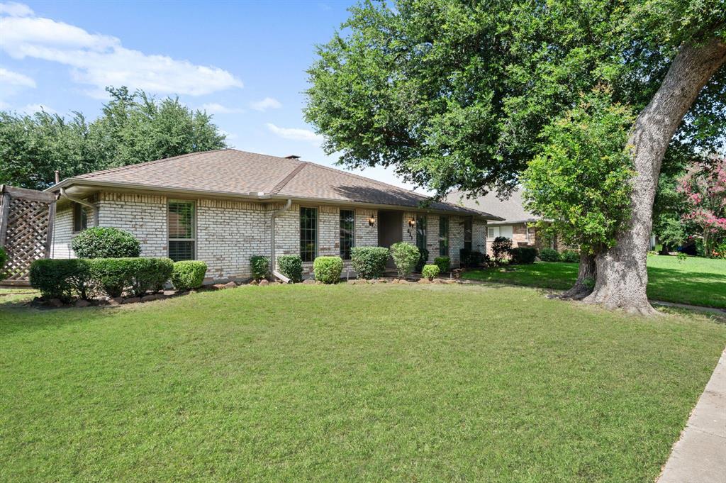 Single-story brick exterior featuring a hipped roof, grid-pattern windows, and established landscaping including a large mature tree and manicured lawn