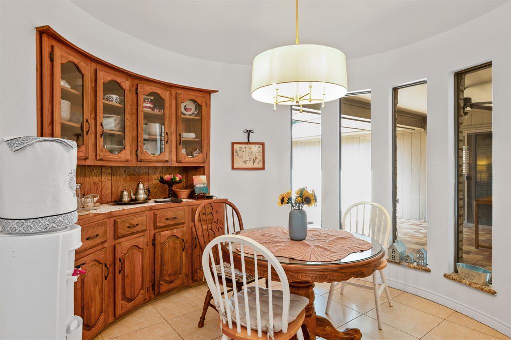 Curved wall architecture featuring built-in wood cabinetry with glass-front display panels, tiled flooring, and a drum-style pendant light fixture