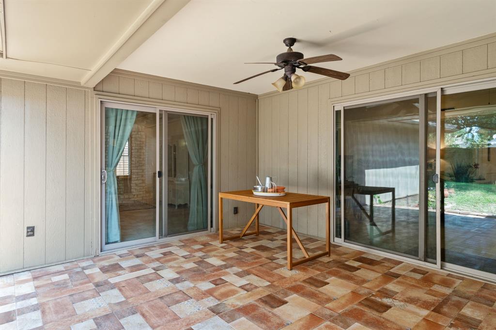 Covered patio featuring multi-toned tile flooring, vertical siding, two sets of glass sliding doors, and a ceiling-mounted fan