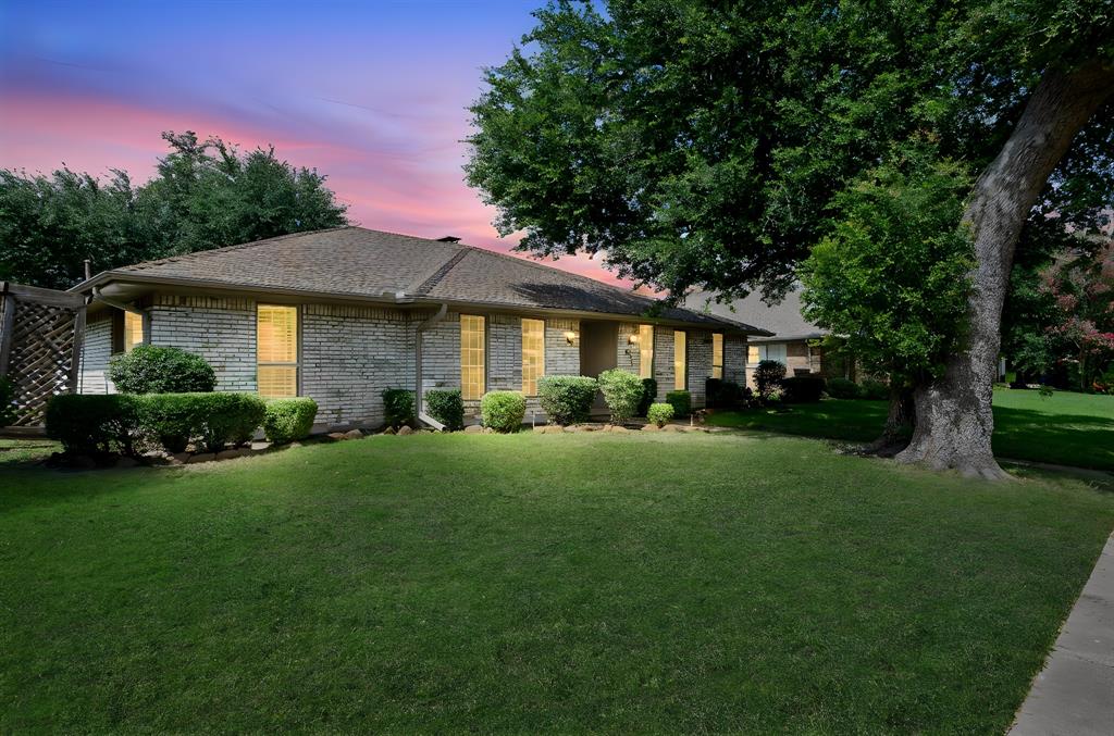 Single-story brick exterior featuring a multi-pitched roofline, mature trees, and manicured landscaping