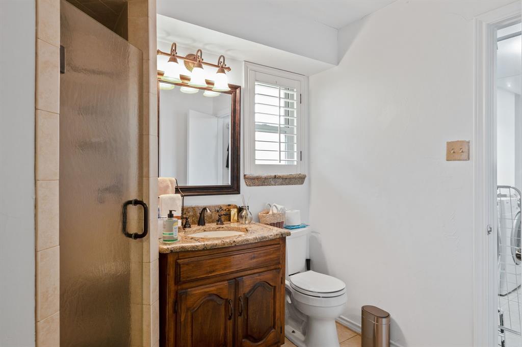 Bathroom featuring a custom wood vanity with a stone countertop, an integrated sink, a framed mirror with a three-light fixture, and a tiled shower stall with a glass door