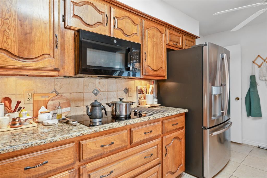 Kitchen featuring wood cabinetry, stone countertops, stone tile backsplash, integrated stainless steel appliances, and a glass cooktop