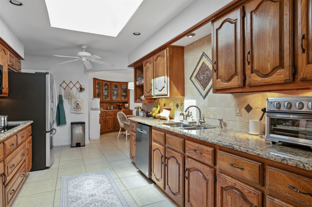 Kitchen featuring wood cabinetry, stone countertops, tiled backsplash with decorative inlay, stainless steel dishwasher, and a skylight