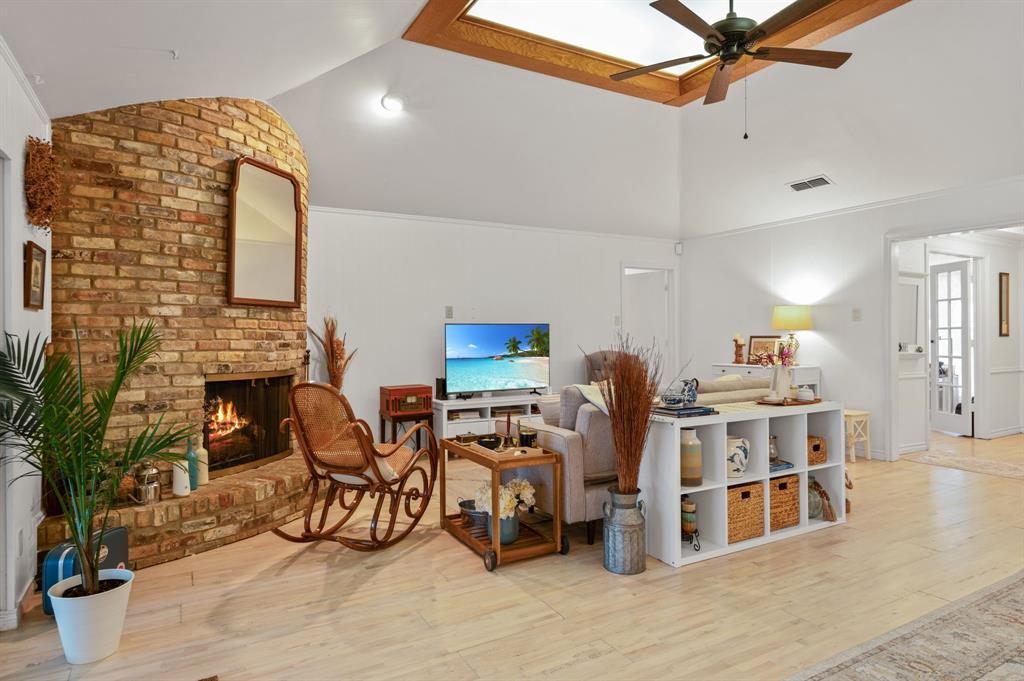 Living area featuring vaulted ceilings, a central skylight with wood trim, a curved brick fireplace, and light-toned wood-finish flooring