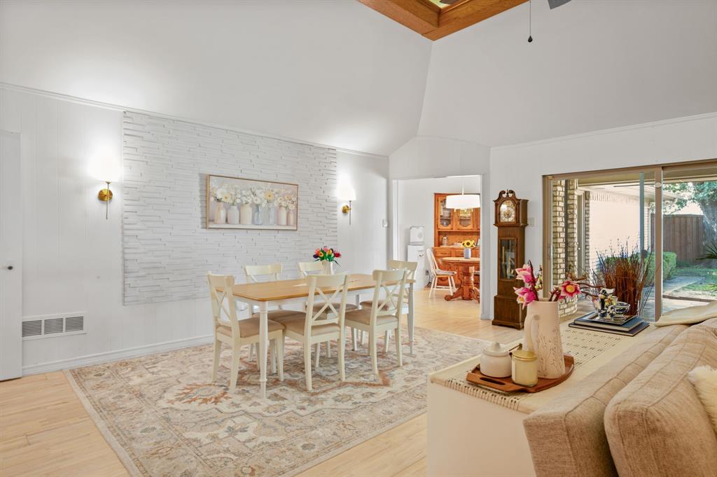 Vaulted ceilings, textured stone accent wall, wood-finish flooring, wall-mounted light fixtures, and sliding glass doors