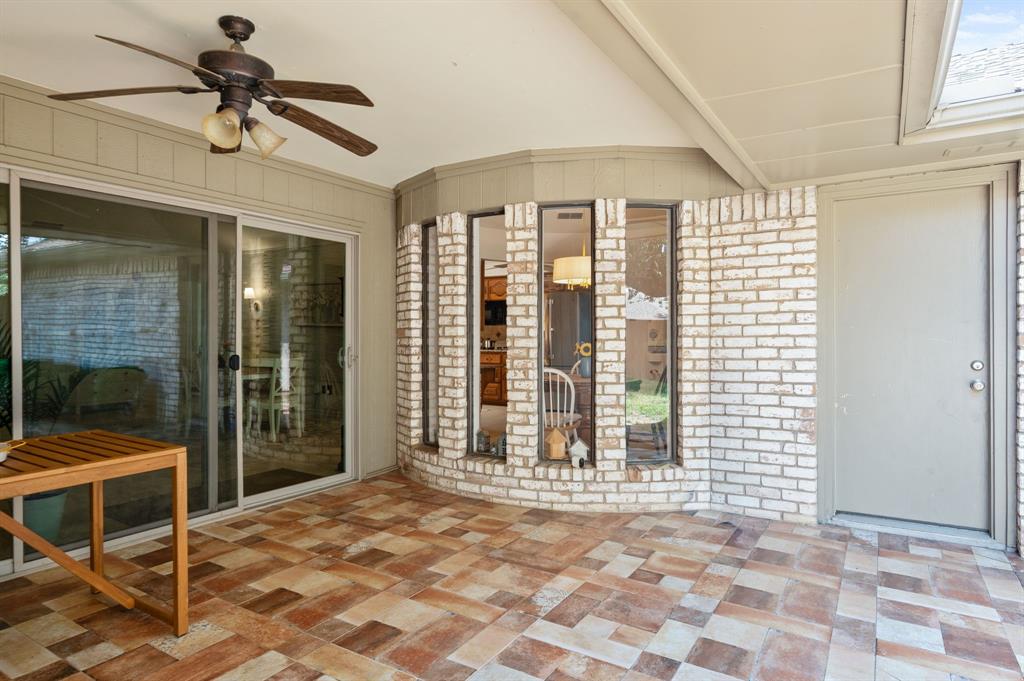 Covered patio featuring a multi-tone tile floor, brick-accented exterior wall, bay window configuration, and a ceiling-mounted fan with integrated lighting