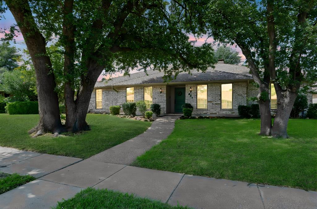 Single-story brick exterior featuring a concrete walkway, gabled roofline, and mature trees on a landscaped lot