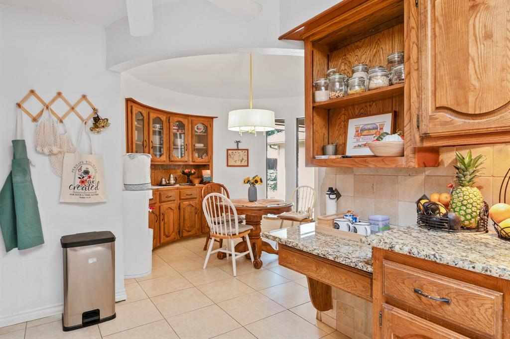Kitchen area featuring natural wood cabinetry, stone countertops, tiled backsplash, ceramic tile flooring, and a semi-circular built-in hutch with glass-front display doors