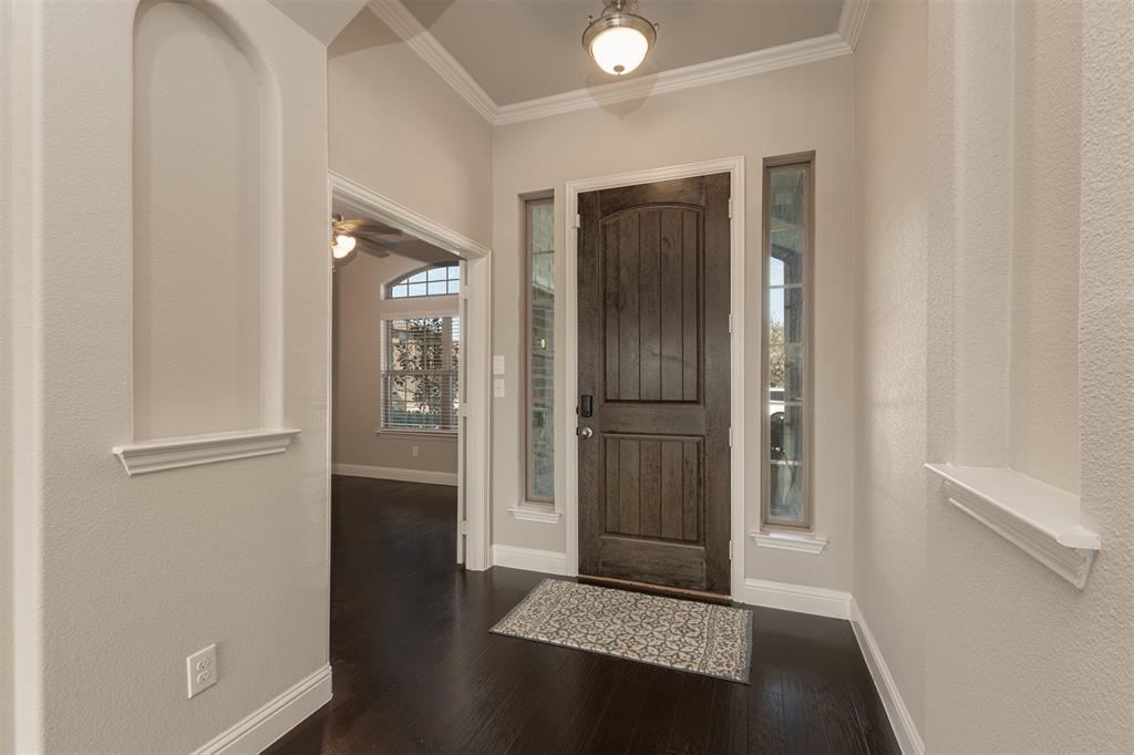 Foyer featuring wood-finish flooring, recessed wall niches, dark-stained wood entry door, sidelight windows, and crown molding