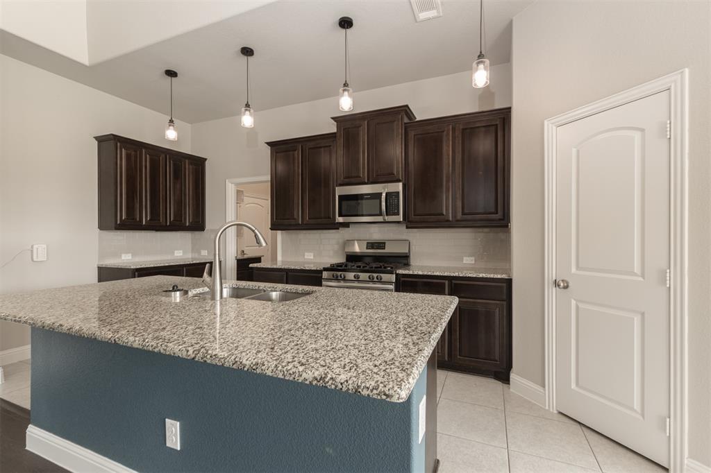 Kitchen featuring dark wood cabinetry, stone-surface countertops, central island, stainless steel appliances, and pendant lighting