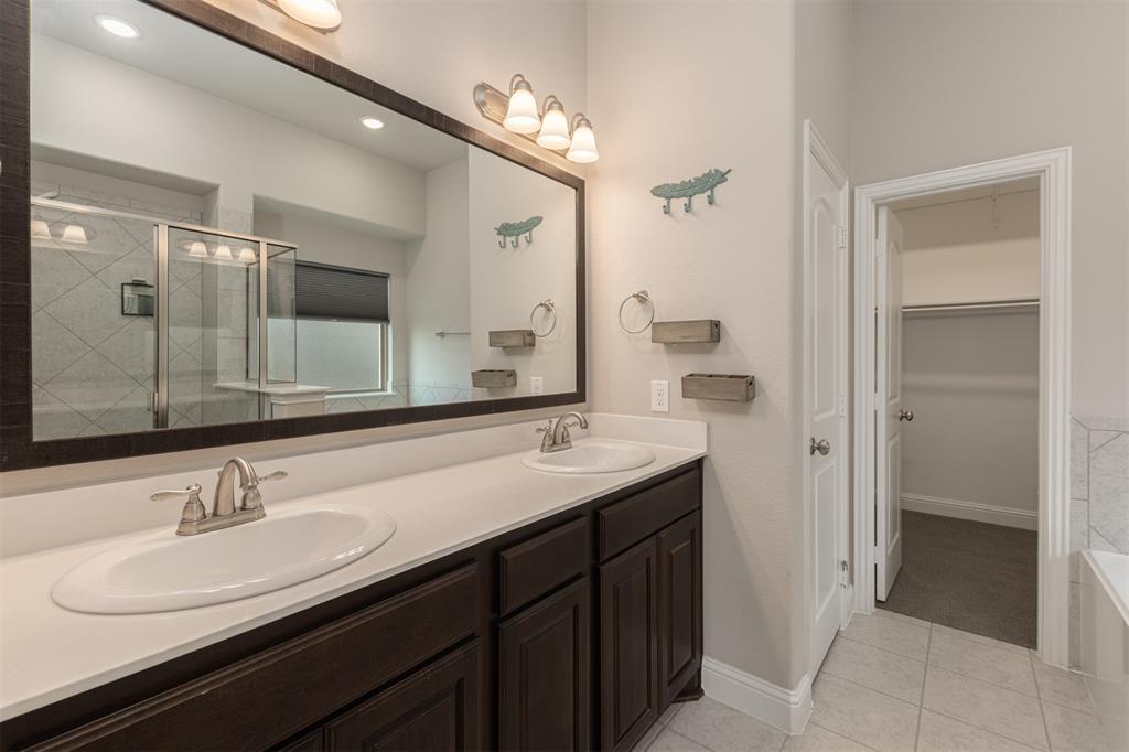 Dual-sink vanity with dark wood cabinetry, solid-surface countertop, full-width mirror, and integrated lighting