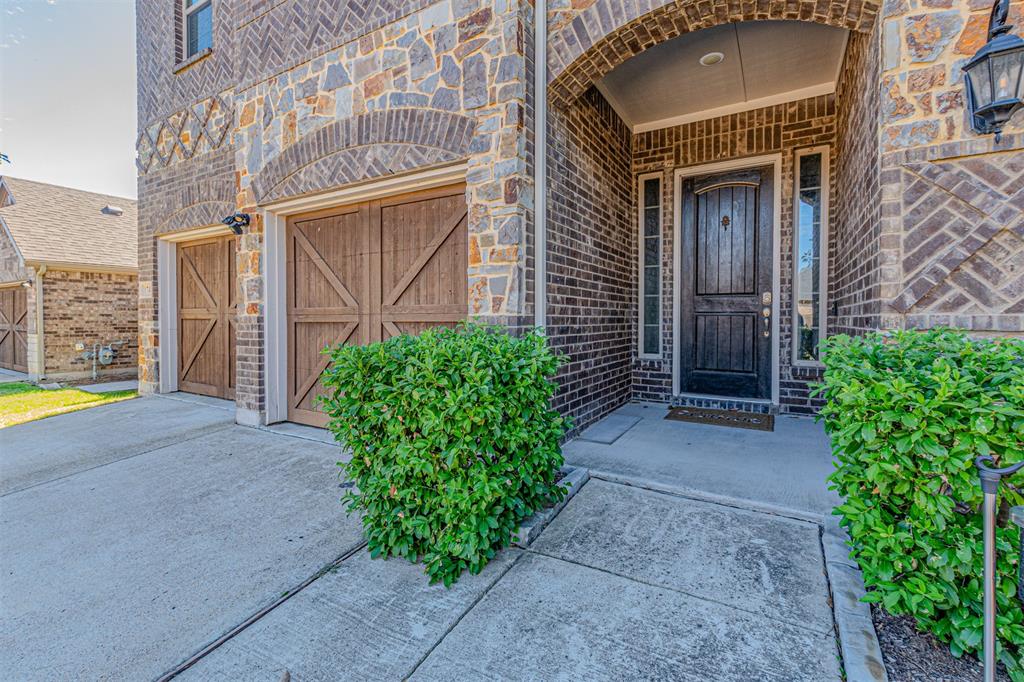 Exterior facade featuring a combination of brick and stone masonry, decorative brickwork accents, wood-finish carriage-style garage doors, a recessed arched entry, and a multi-paneled dark wood entry door with side windows
