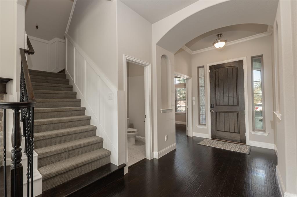 Foyer featuring a dark-finish wooden door with glass sidelights, an arched entryway, dark wood-finish flooring, and a staircase with carpeted treads and an iron baluster