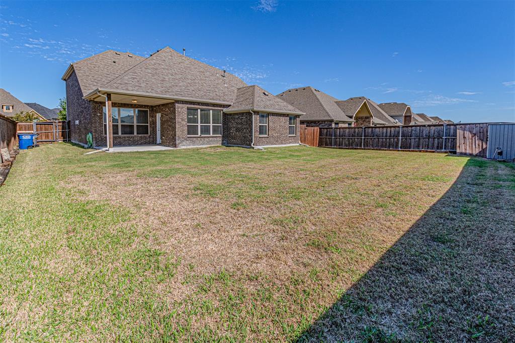 Brick exterior featuring a covered rear patio, expansive lawn, and full wood privacy fencing