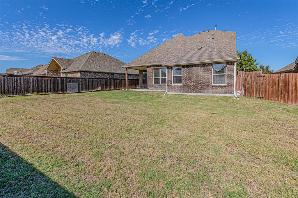 Rear exterior featuring brick masonry construction, a covered patio, and a fenced backyard