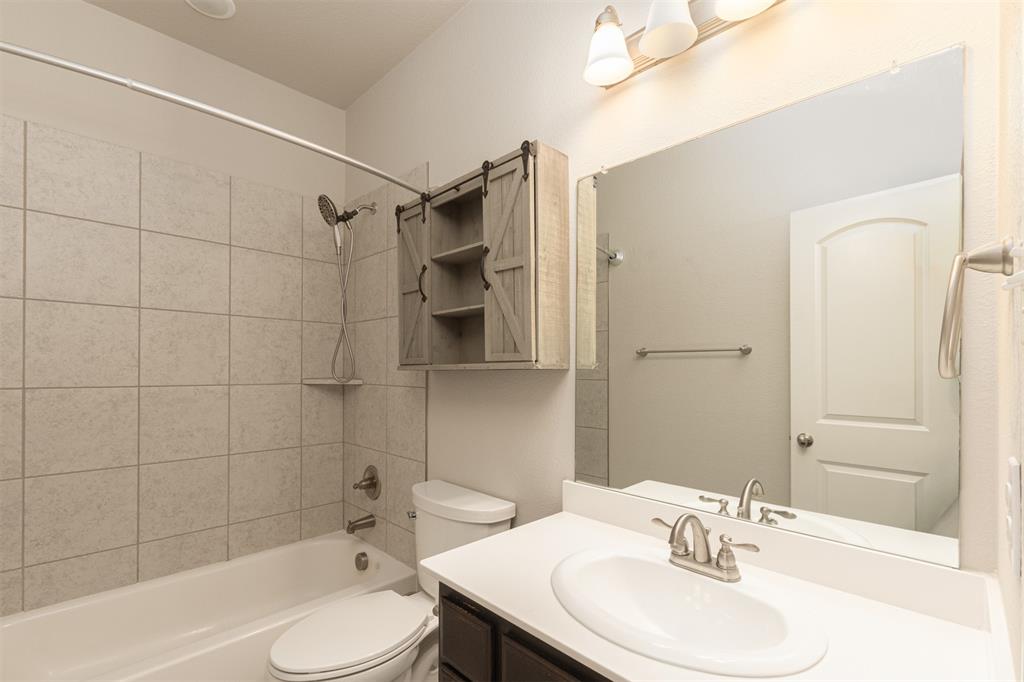 Bathroom featuring a white vanity with an integrated sink, large wall-mounted mirror, sliding barn-door style cabinetry, and a shower-tub combination with tiled surround