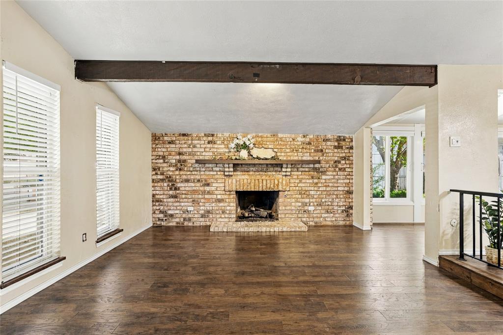 Inviting living room with vaulted ceilings, exposed wood beams, wood-look flooring, and a striking brick fireplace.