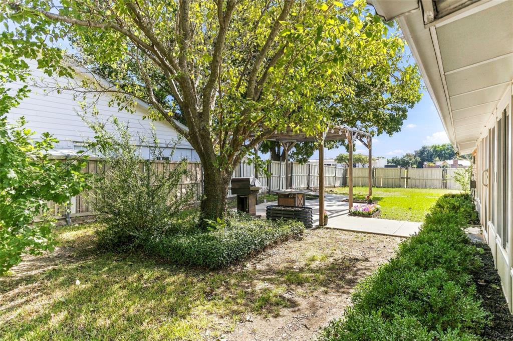 Rear and side exterior view highlighting the brick exterior, mature shade trees, and expansive backyard with privacy fencing.