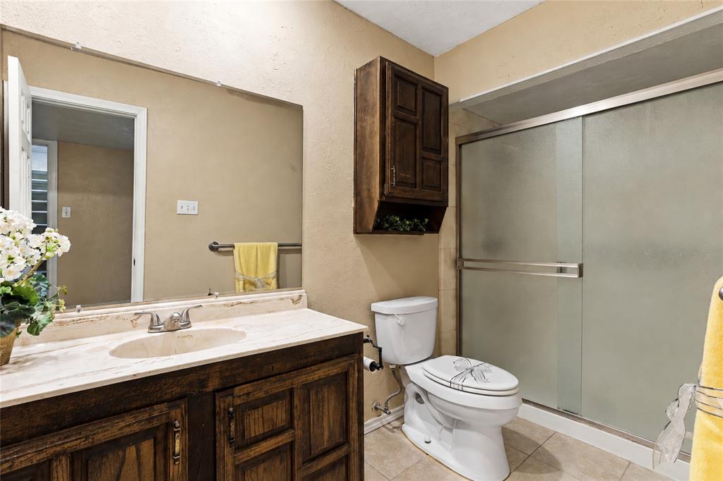 Bathroom featuring a wood-finish vanity, ample countertop space, a walk in shower, and neutral finishes.