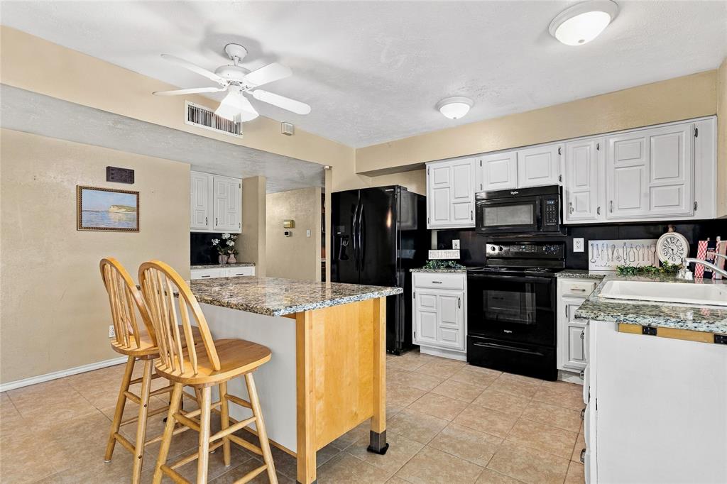 Kitchen featuring white cabinetry, black appliances, a center island with seating, and ample counter space.