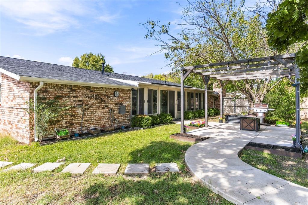 Backyard view showcasing the brick exterior, covered patio area, storage shed, mature trees, and grassy lawn.