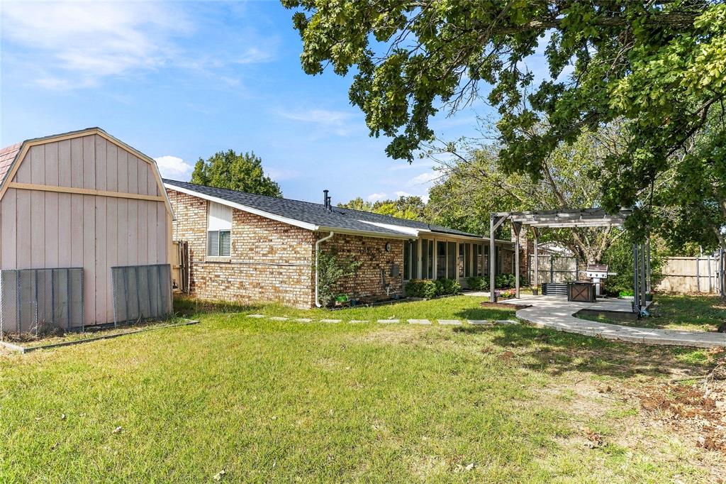 Backyard featuring a curved concrete walkway, covered patio, brick exterior, and established landscaping.