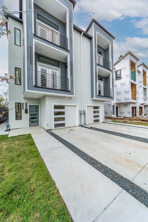 Contemporary three-story exterior featuring a smooth stucco finish, dual-level balconies with metal railings, and a multi-pane glass garage door