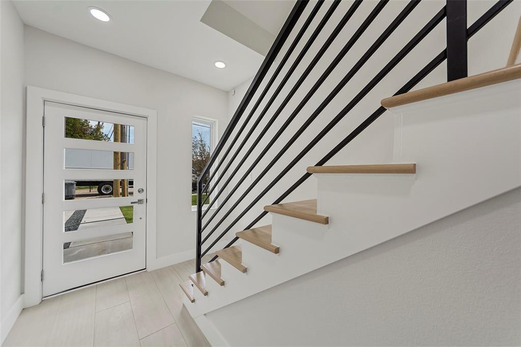 Entryway featuring a white door with horizontal glass panels, recessed ceiling lighting, light-toned tile flooring, and a staircase with wood-finish treads and a matte black metal railing Entryway featuring a white door with horizontal glass panels, recessed ceiling lighting, light-toned tile flooring, and a staircase with wood-finish treads and a matte black metal railing