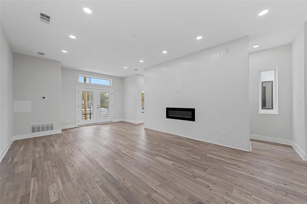 Interior space featuring wood-finish flooring, recessed lighting, double glass-paneled doors, and a floor-to-ceiling accent wall with an integrated linear fireplace