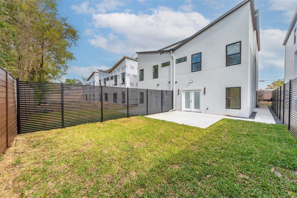 Contemporary white exterior with dual-pitched rooflines, featuring a concrete patio, horizontal slat perimeter fencing, and manicured turf