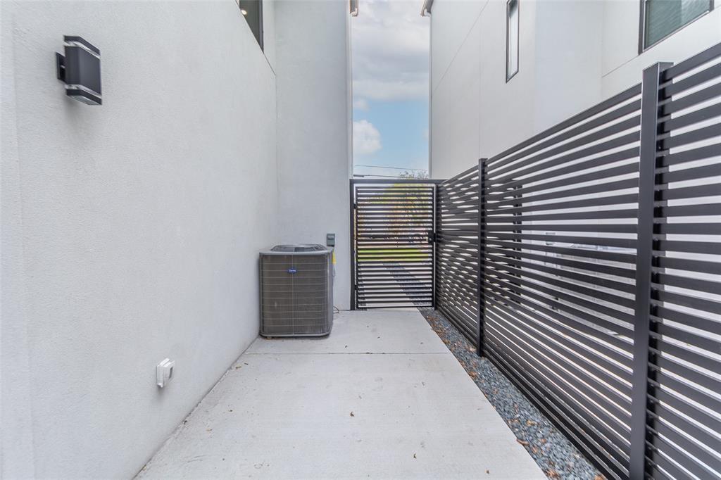 Side yard featuring smooth stucco walls, black metal horizontal-slat fencing, a concrete walkway, and wall-mounted exterior lighting