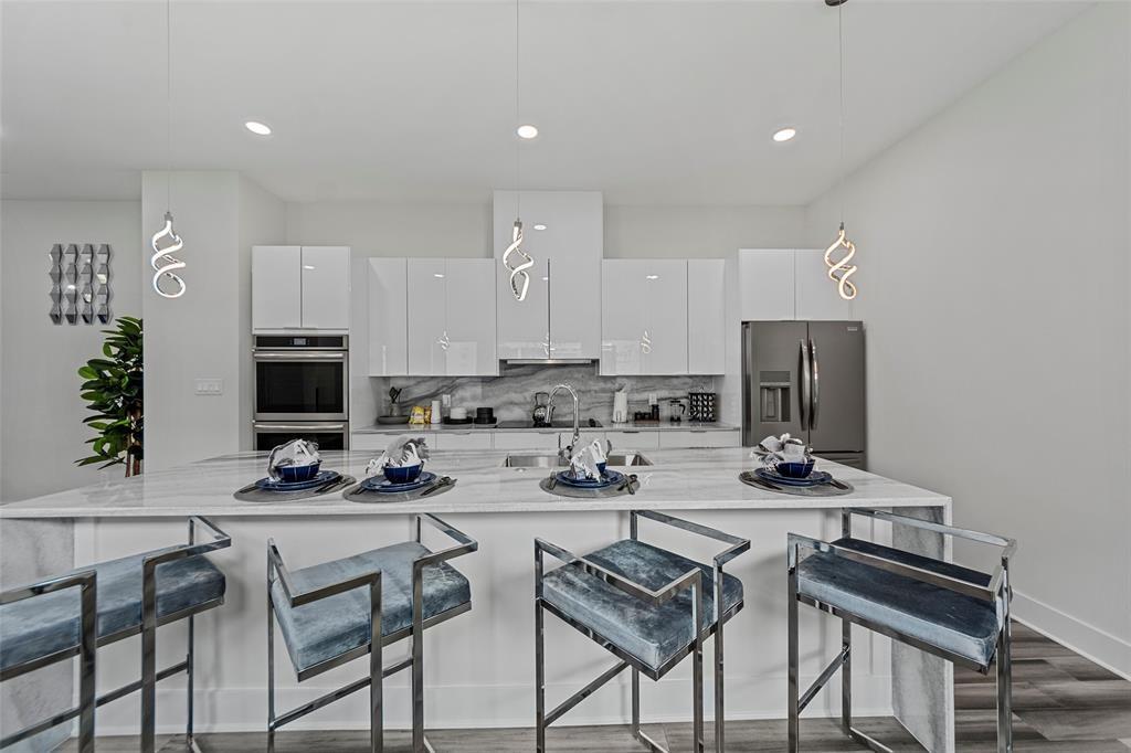 Modern kitchen featuring high-gloss white cabinetry, a stone-patterned island with waterfall edges, built-in stainless steel double ovens, and decorative pendant lighting
