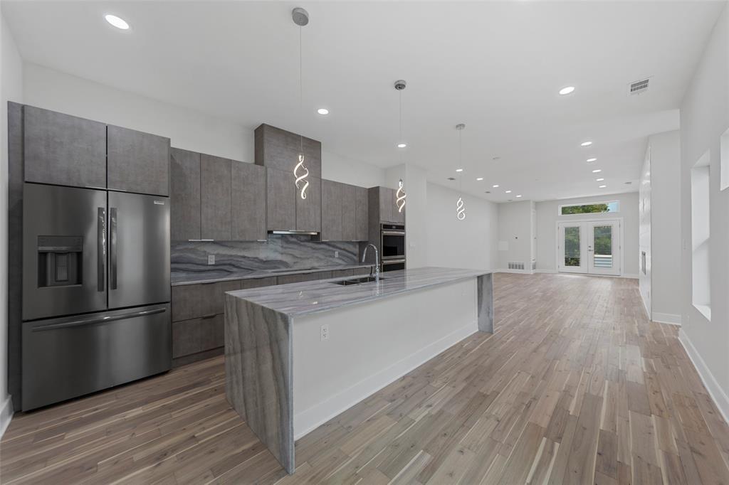 Modern kitchen featuring a waterfall-edge stone island, flat-panel cabinetry, stainless steel appliances, pendant lighting, and wood-finish flooring