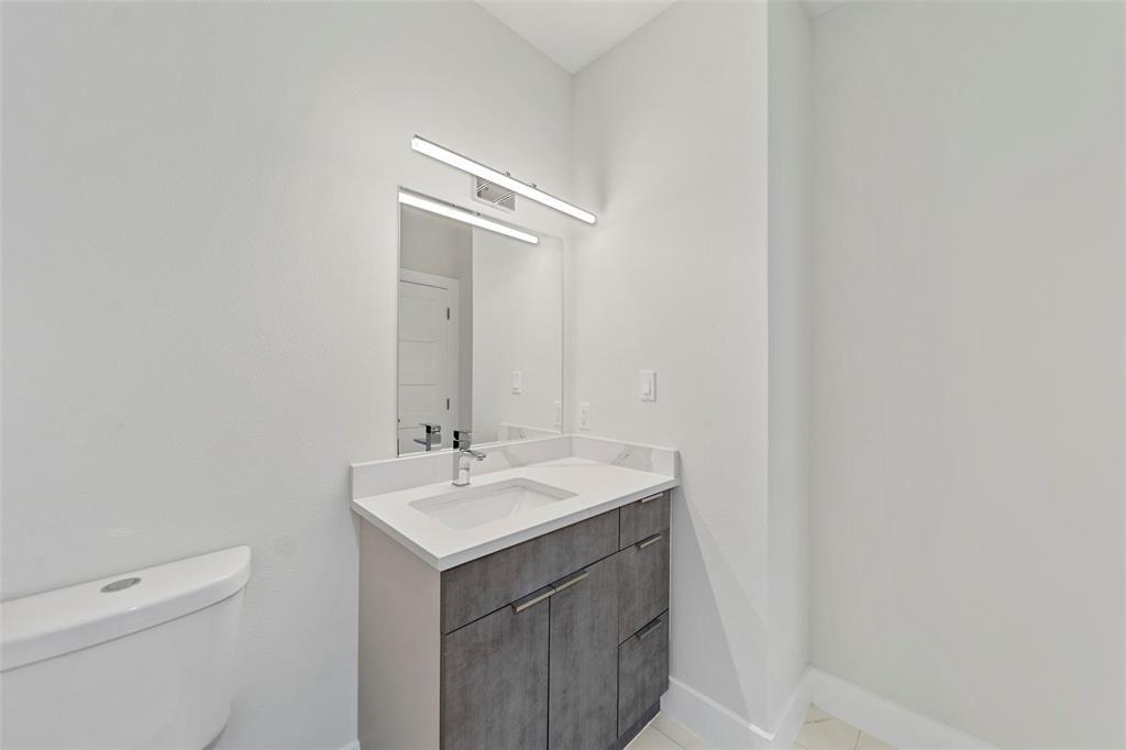 Modern vanity featuring a stone-composite countertop, rectangular undermount sink, chrome faucet, grey textured cabinetry, and wall-mounted linear LED lighting