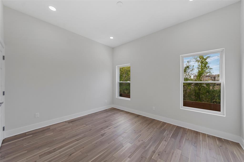 High-ceiling room featuring neutral paint, wood-finish flooring, and two double-hung windows with exterior scenery