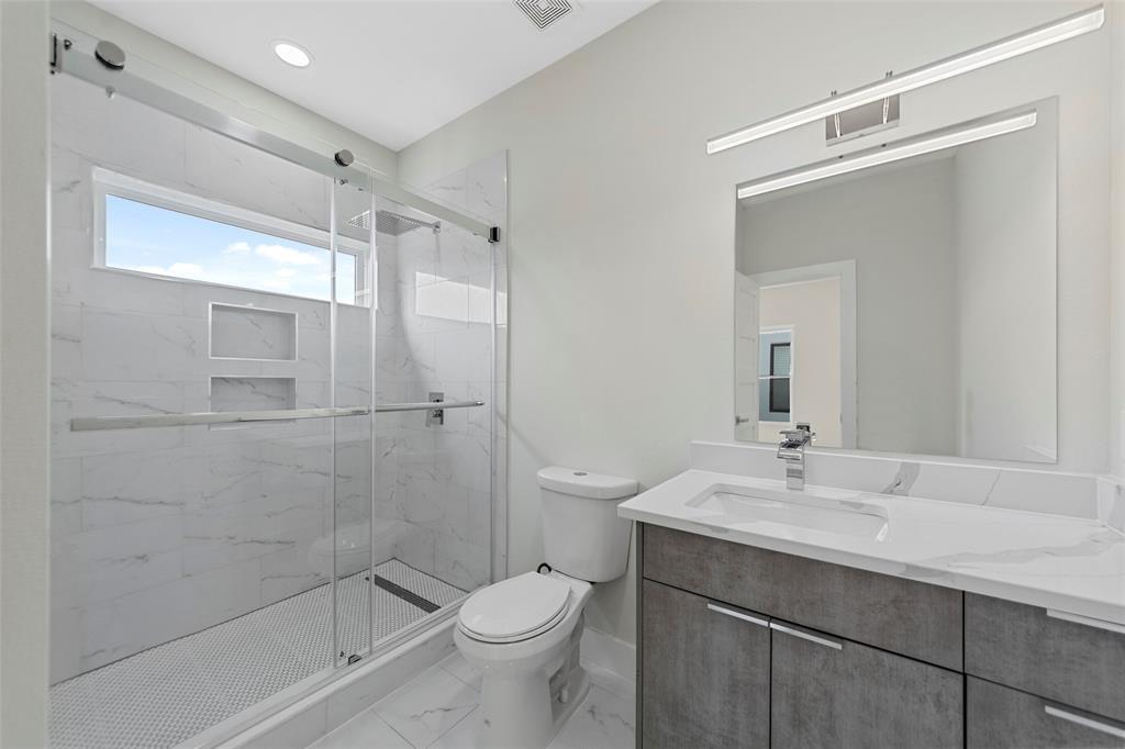 Bathroom featuring a vanity with stone-finish countertop, walk-in shower with sliding glass doors, dual recessed shower niches, and polished chrome fixtures