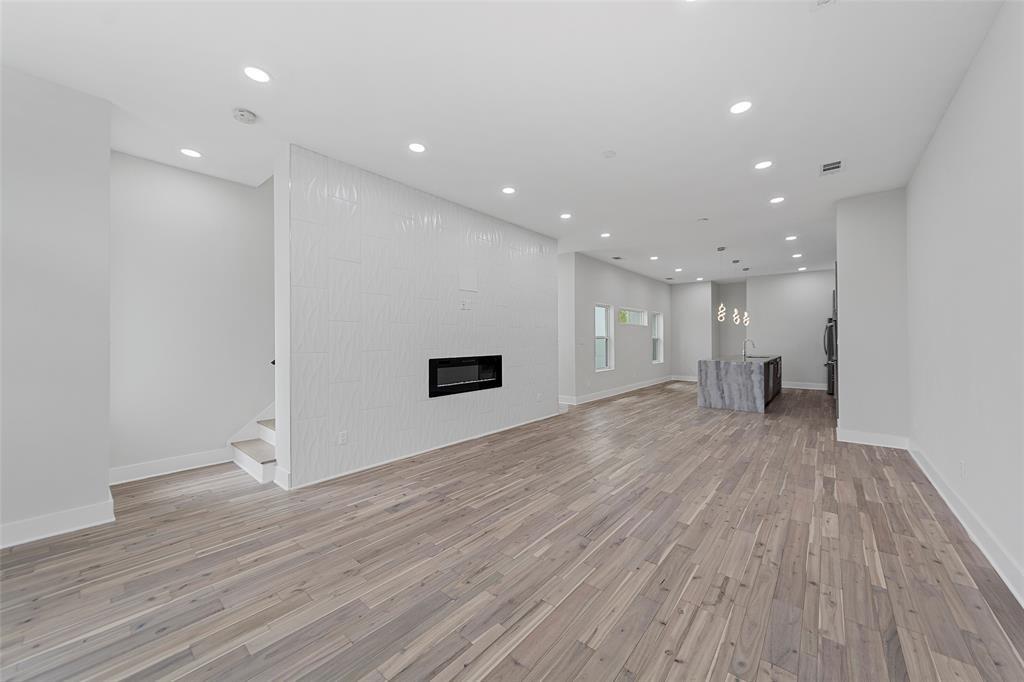 Open floor plan featuring wood-finish flooring, recessed lighting, a fireplace with a textured accent wall, and a kitchen island with stone-finish surfaces