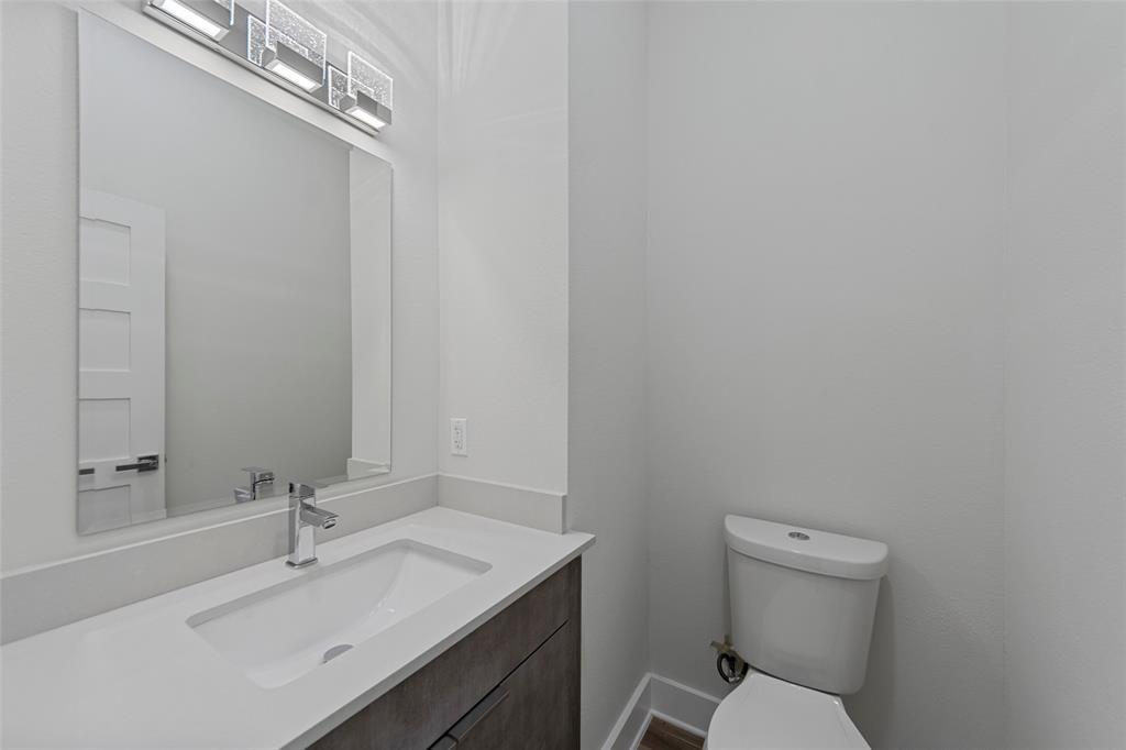 Vanity with a solid-surface countertop and integrated sink, sleek dark-toned cabinetry, rectangular mirror, contemporary linear light fixture, and ceramic toilet