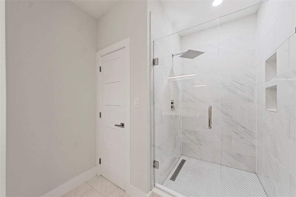 Walk-in shower featuring a frameless glass enclosure, floor-to-ceiling stone-patterned tile, integrated recessed shelving, and a linear drain
