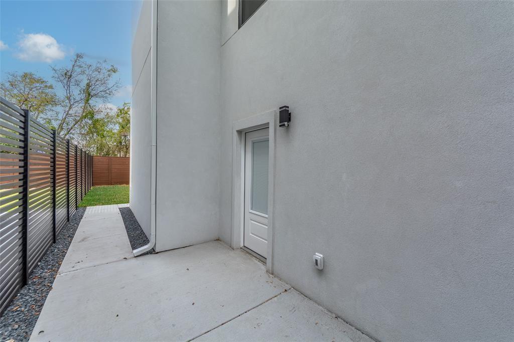 Smooth stucco exterior featuring a single-panel glass-insert entry door, concrete pathway, decorative gravel border, and horizontal slat privacy fencing