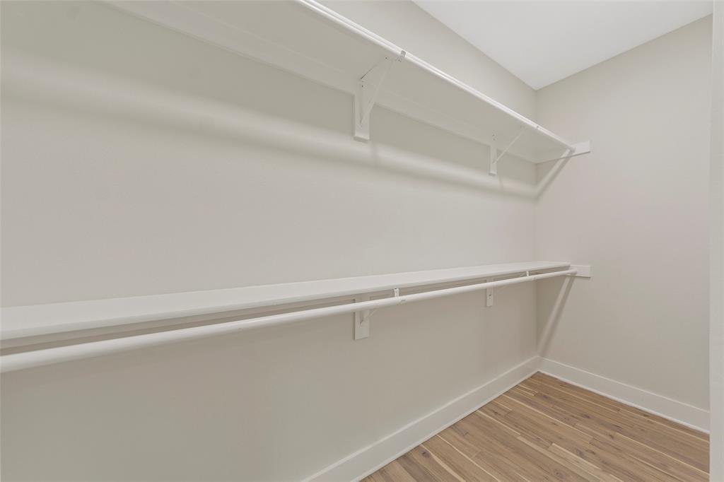 Walk-in closet featuring tiered shelving, integrated clothing rods, and wood-finish flooring